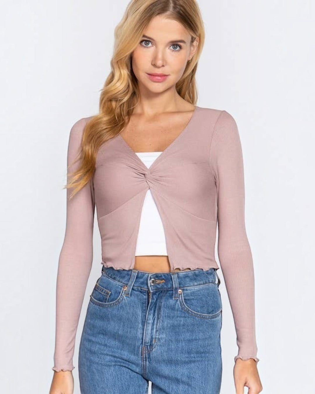 Woman wearing a pink long-sleeve top with a white underlayer and blue jeans on a white background
