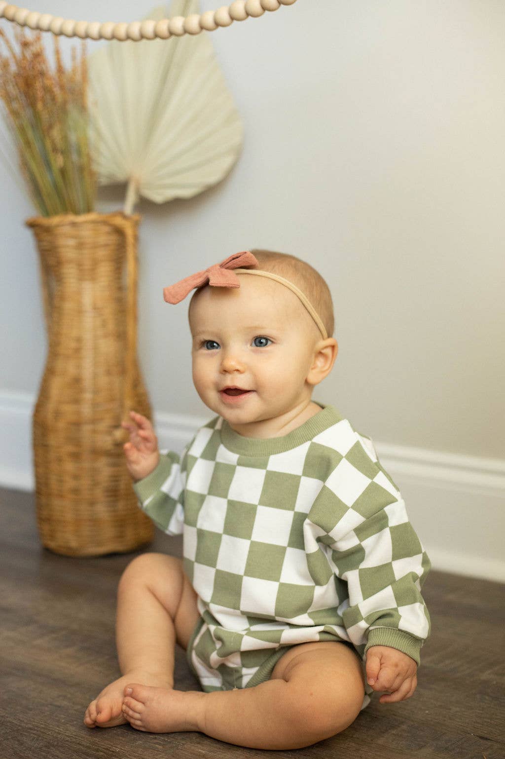 Baby wearing a green and white checkered outfit sitting on the floor.