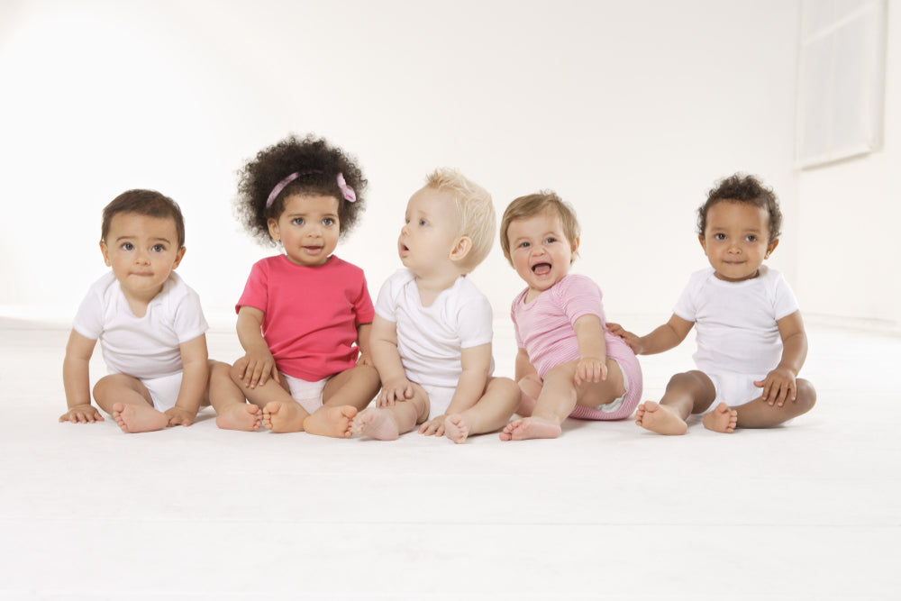 Five babies of various ethnicities sitting together on a white background