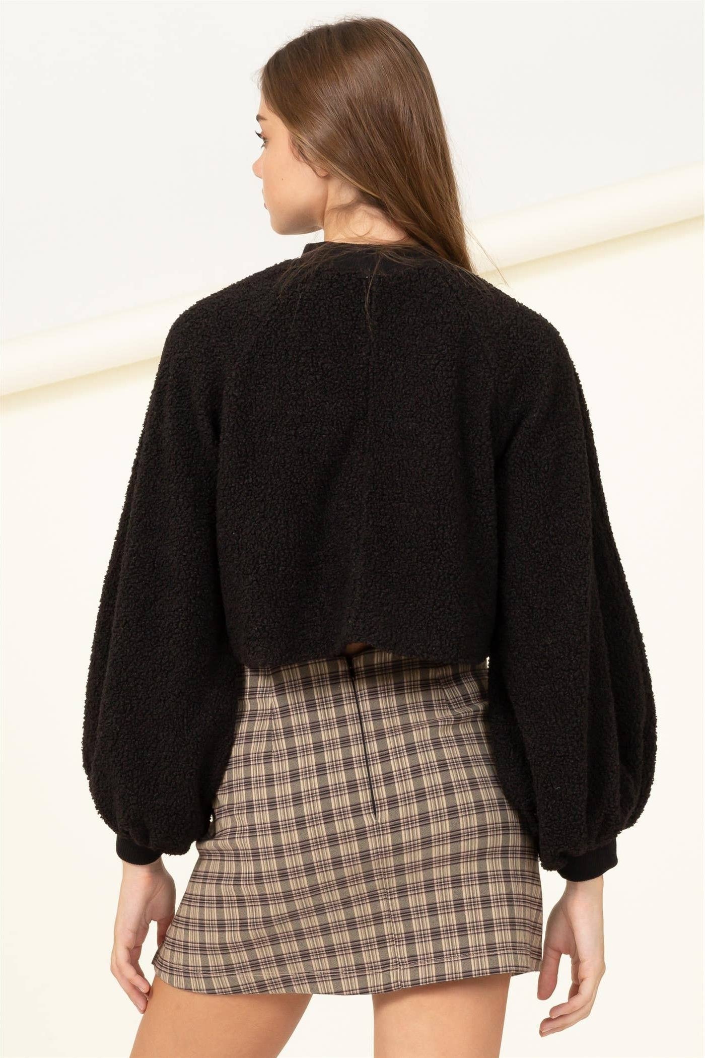 Person wearing a black sweater and plaid skirt on a white background