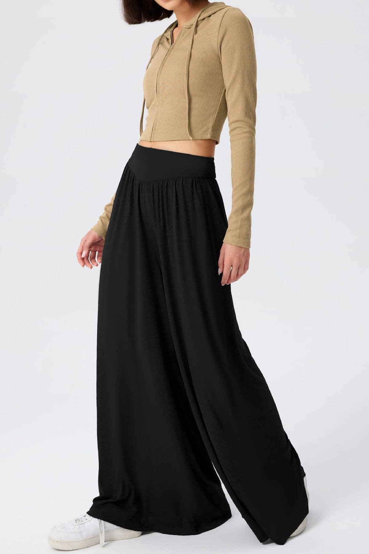 Person wearing a beige cropped hoodie and black wide-leg pants on a white background