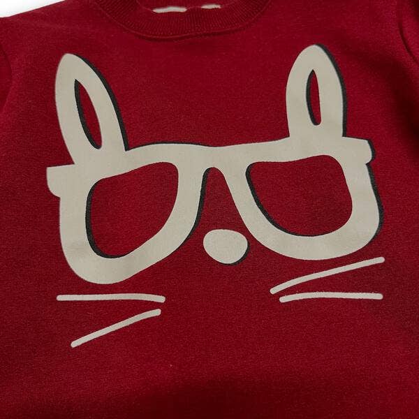 Red shirt with a beige cat face design on a plain background