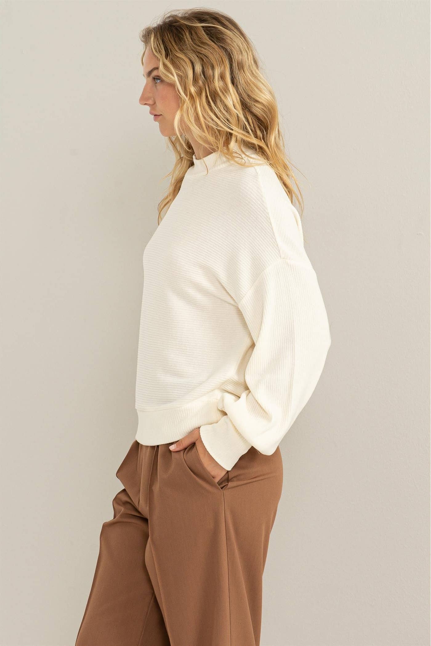 Woman wearing a white blouse and brown pants against a plain background