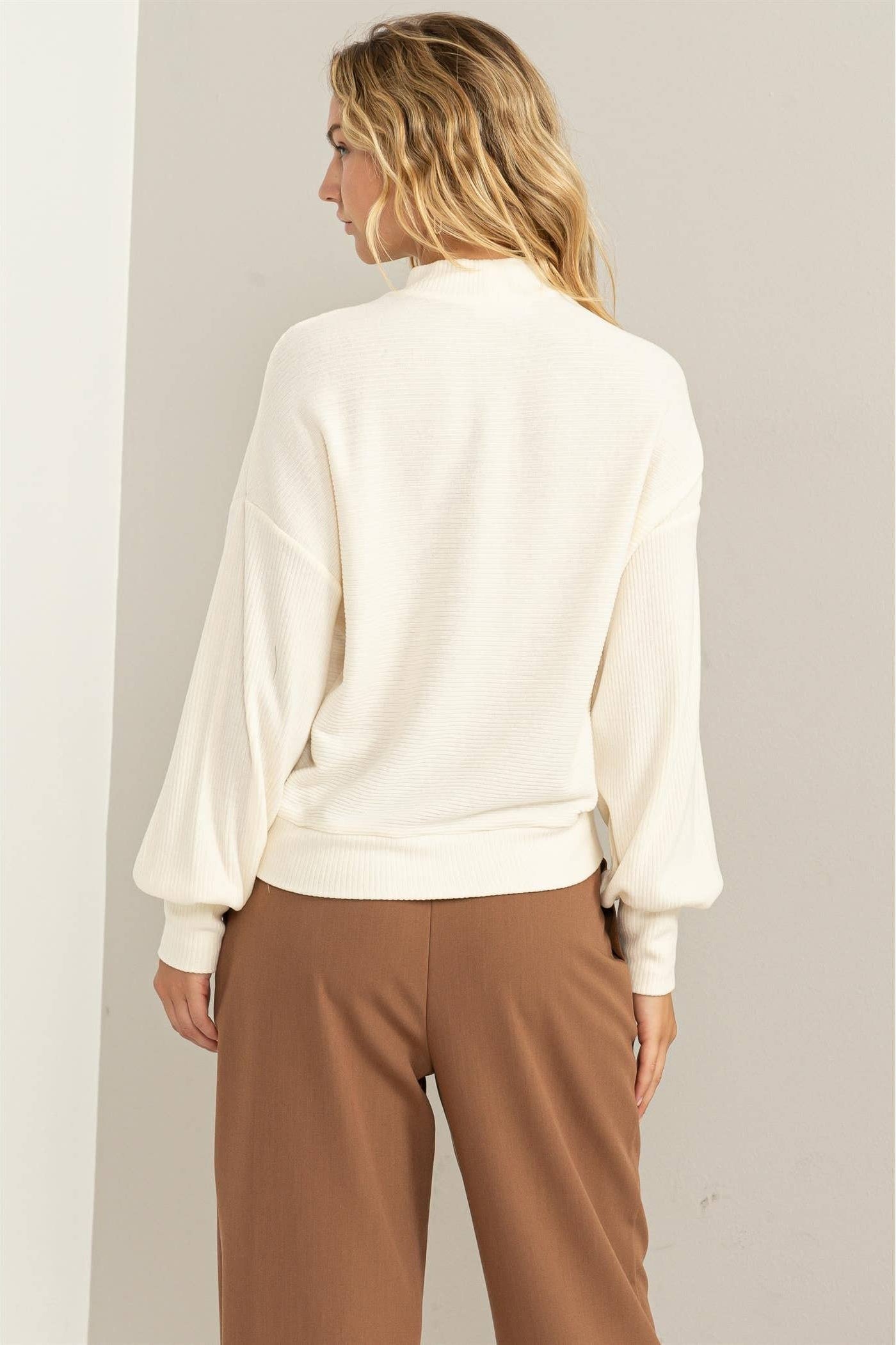 Woman wearing a white blouse and brown pants against a plain background