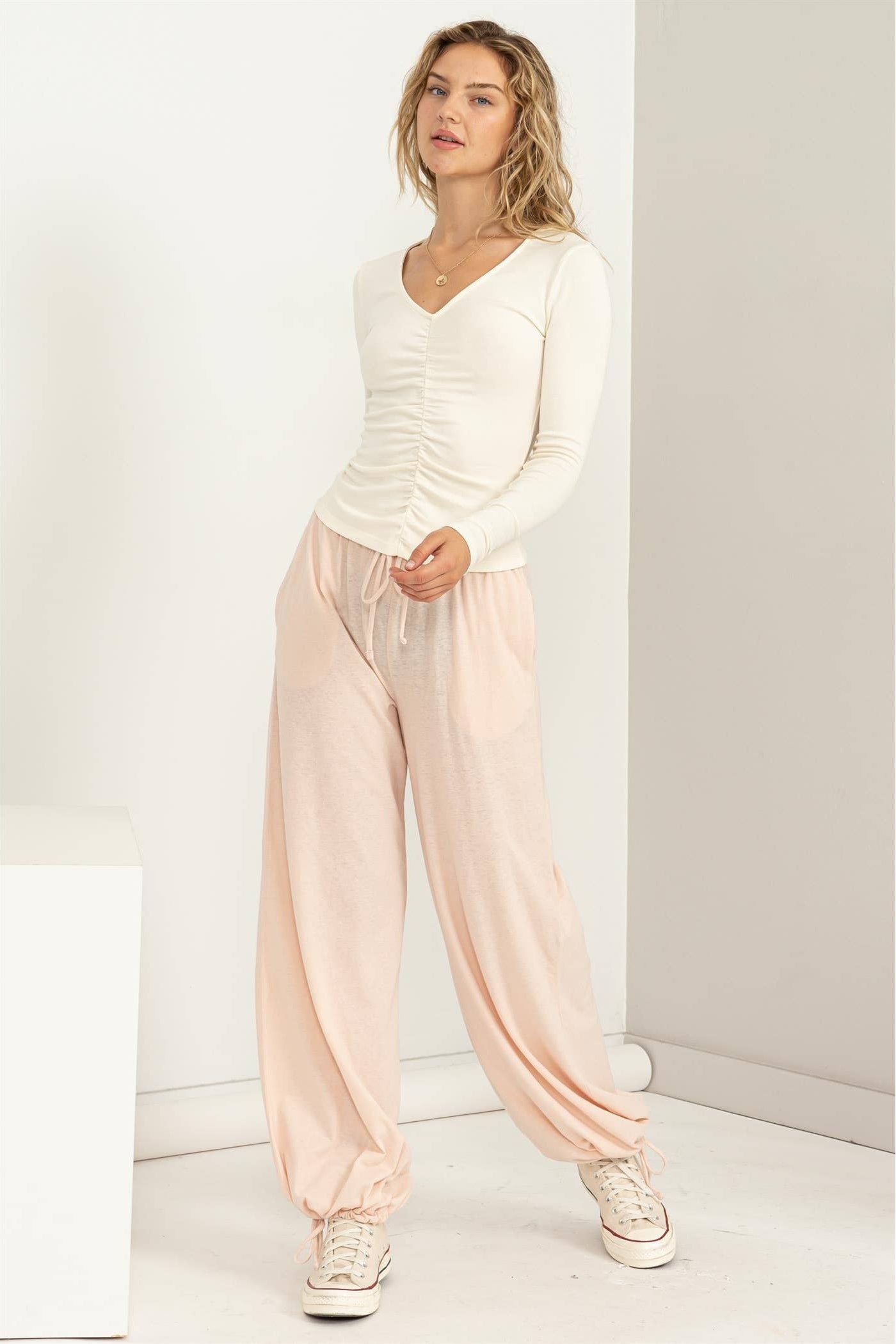 Woman wearing a white top and light pink pants in a minimalistic setting