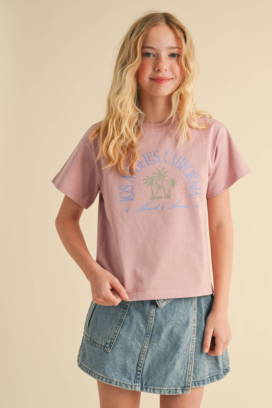 Young girl wearing a pink graphic t-shirt and denim skirt on a beige background