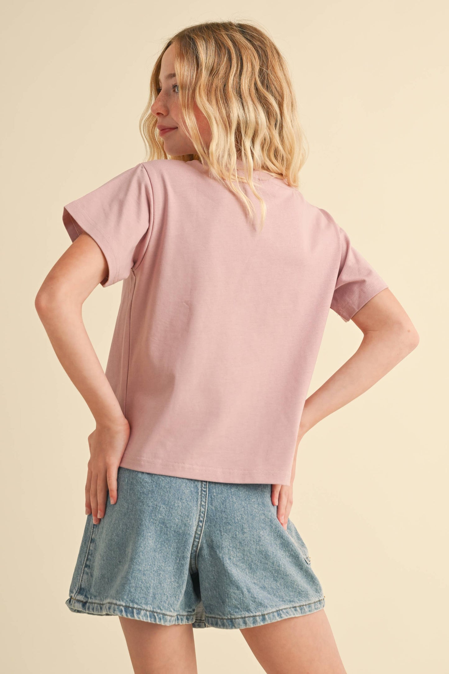 Woman wearing a pink t-shirt and denim shorts on a beige background