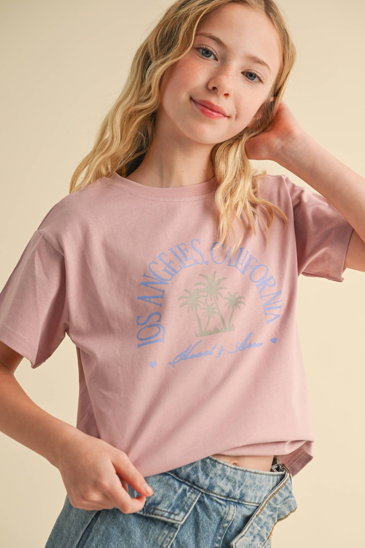 Young girl wearing a pink t-shirt with a palm tree graphic on a beige background