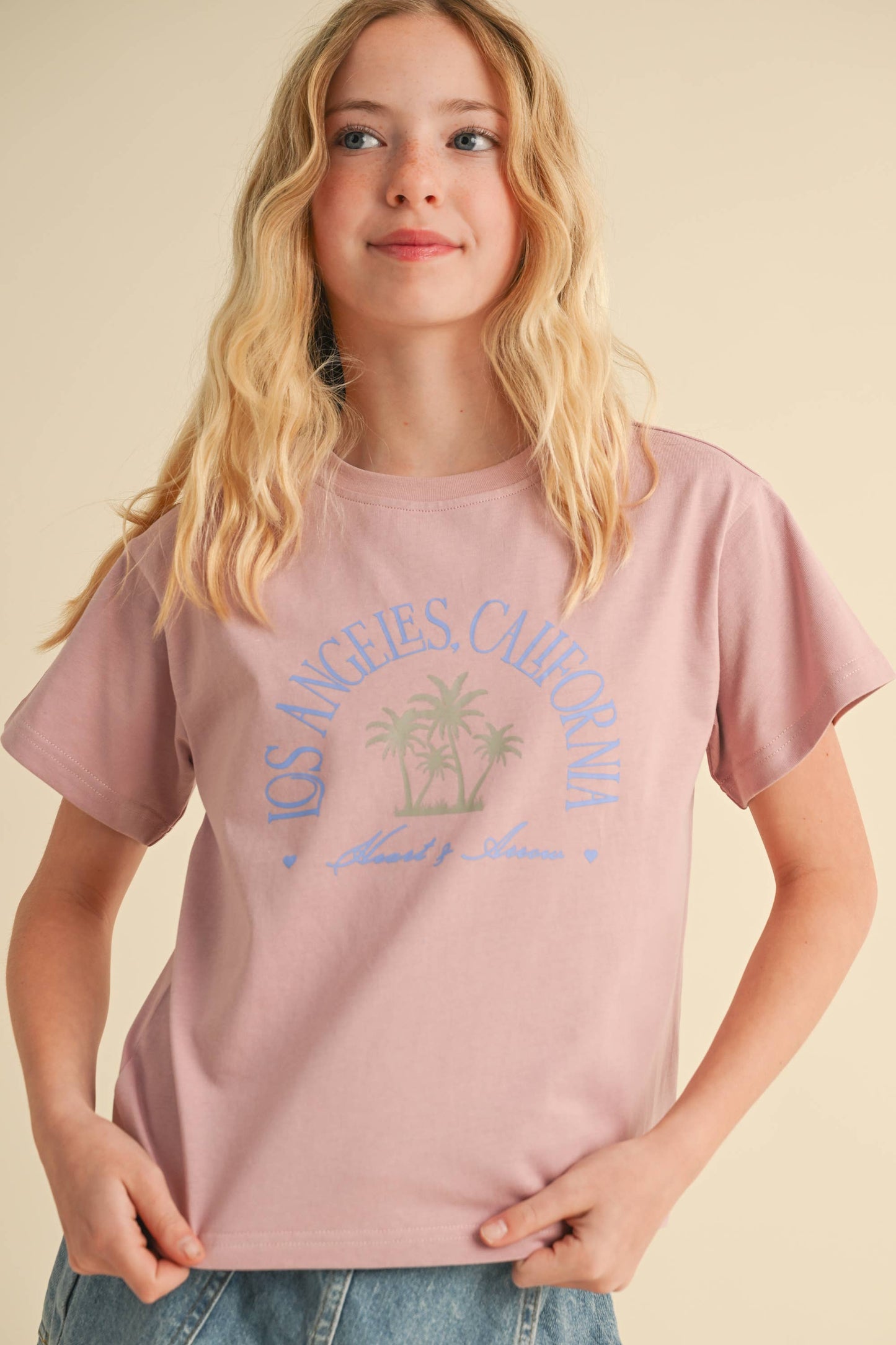 Person wearing a pink t-shirt with 'Los Angeles California' text and palm tree graphics on a beige background