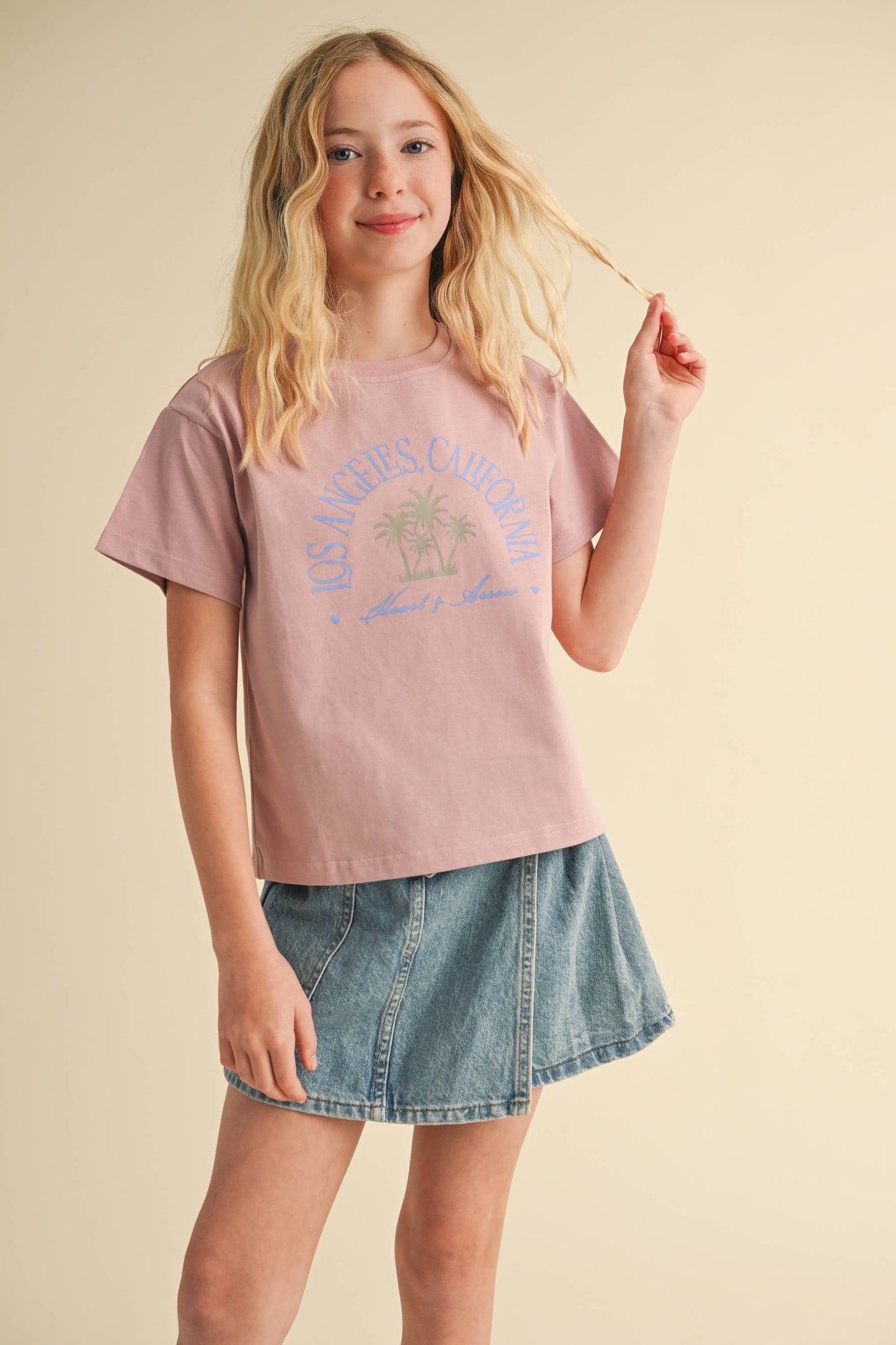 Young girl wearing a pink graphic t-shirt and denim skirt on a beige background
