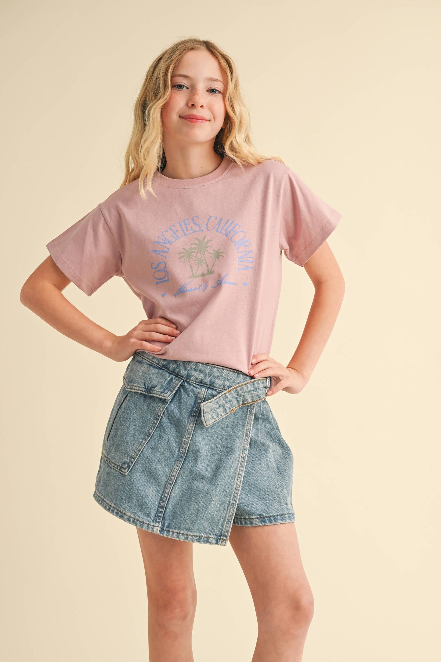 Woman wearing a pink graphic t-shirt and denim skirt on a beige background