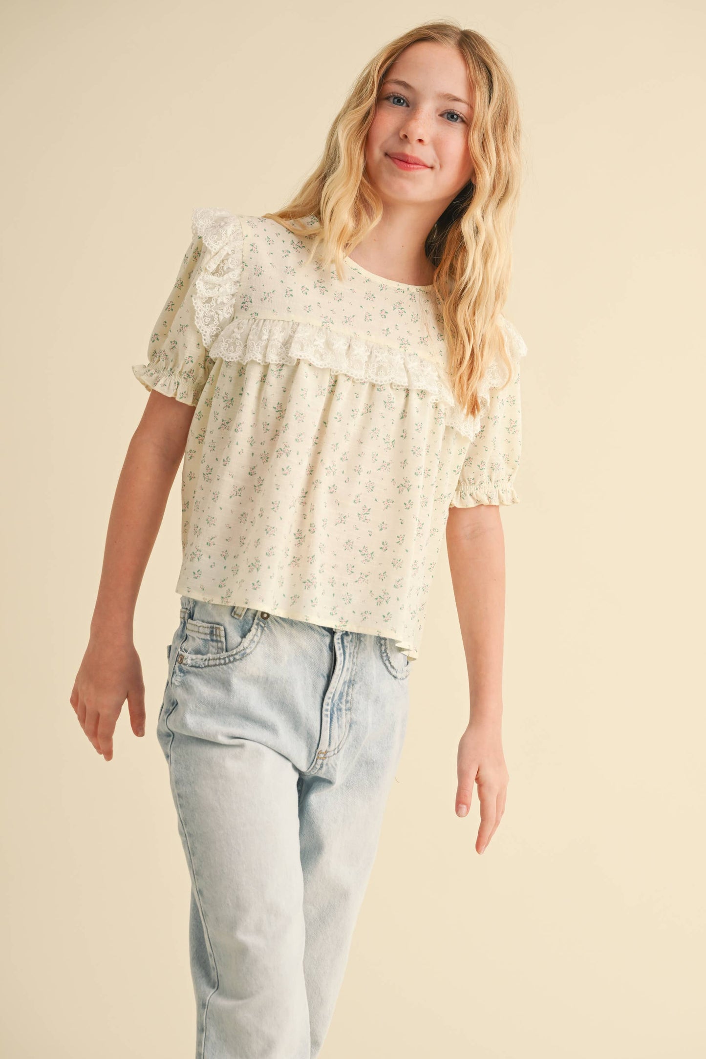 Woman wearing a light-colored blouse with ruffled layers and light blue jeans on a beige background