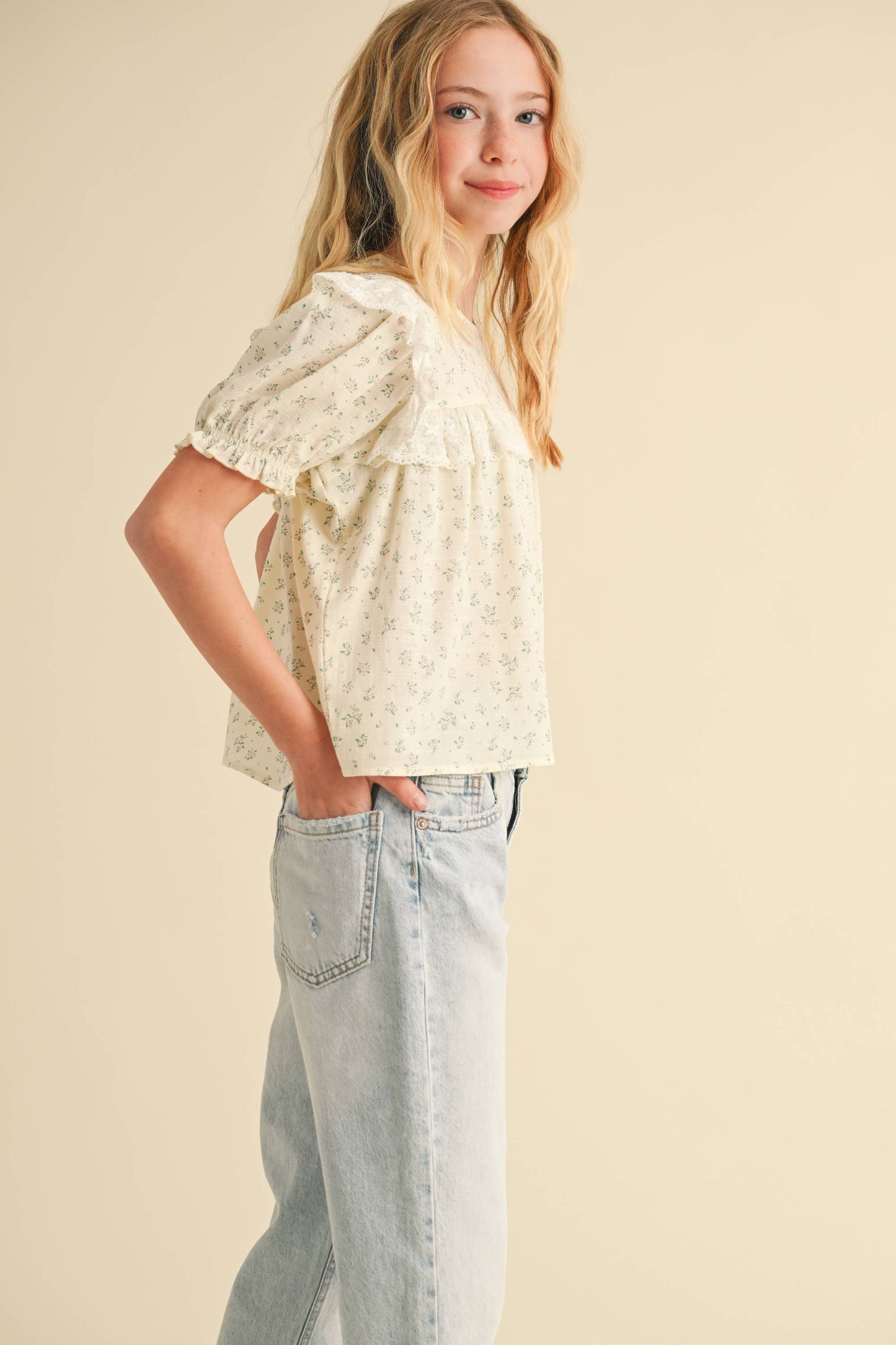 Woman wearing a light-colored floral blouse and jeans against a beige background