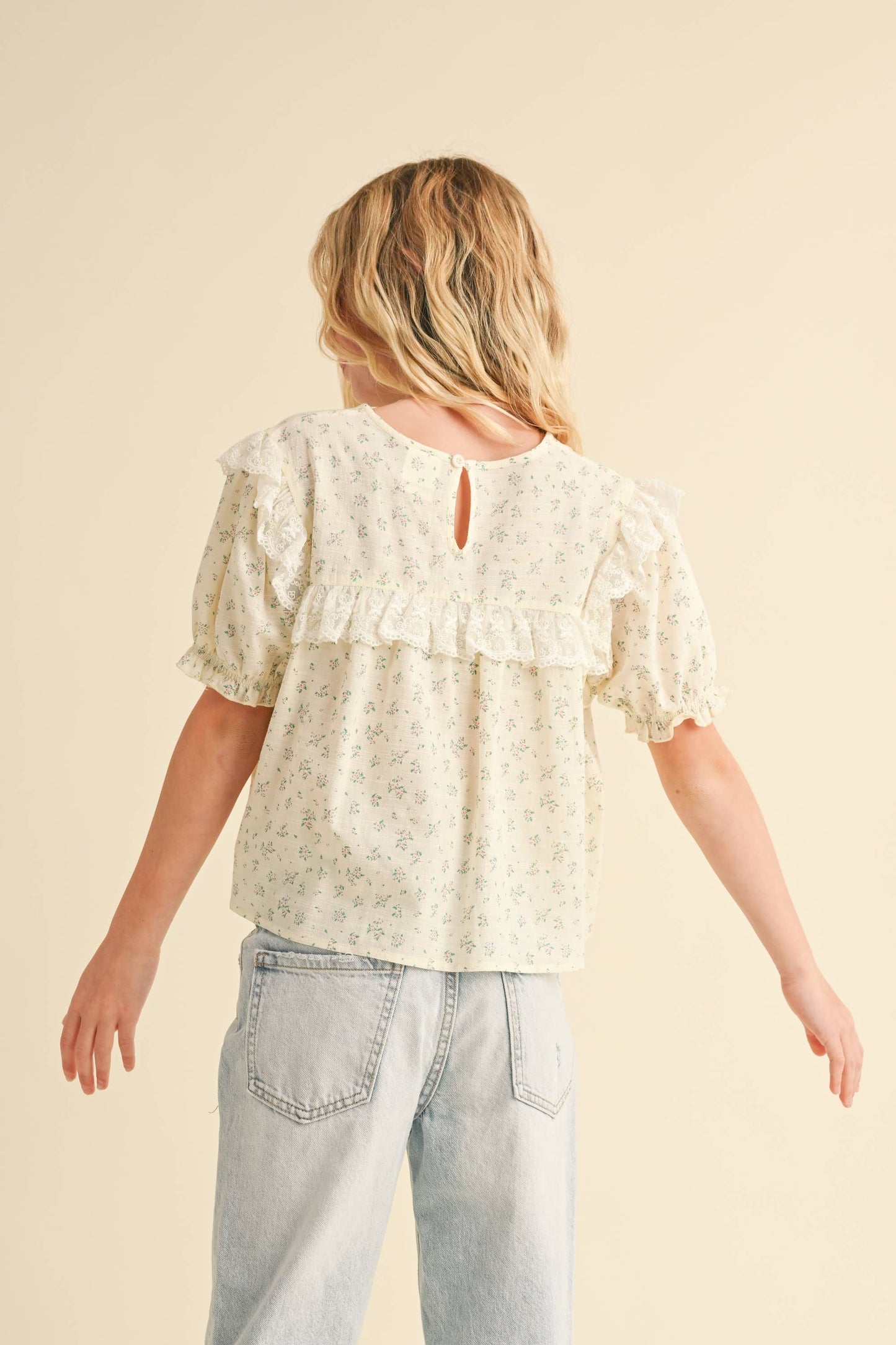 Woman wearing a light-colored lace blouse and jeans on a beige background