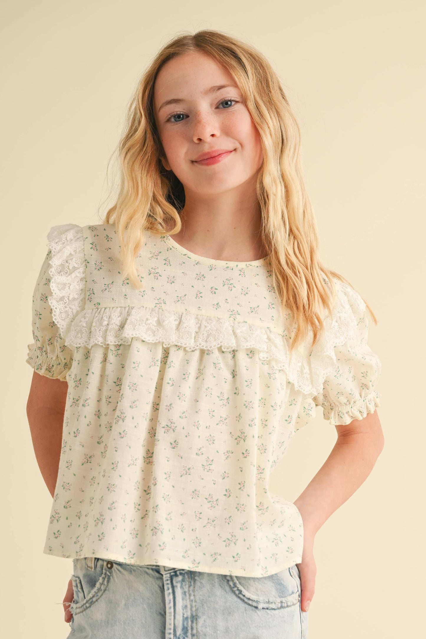 Young girl wearing a floral blouse with puffed sleeves against a beige background
