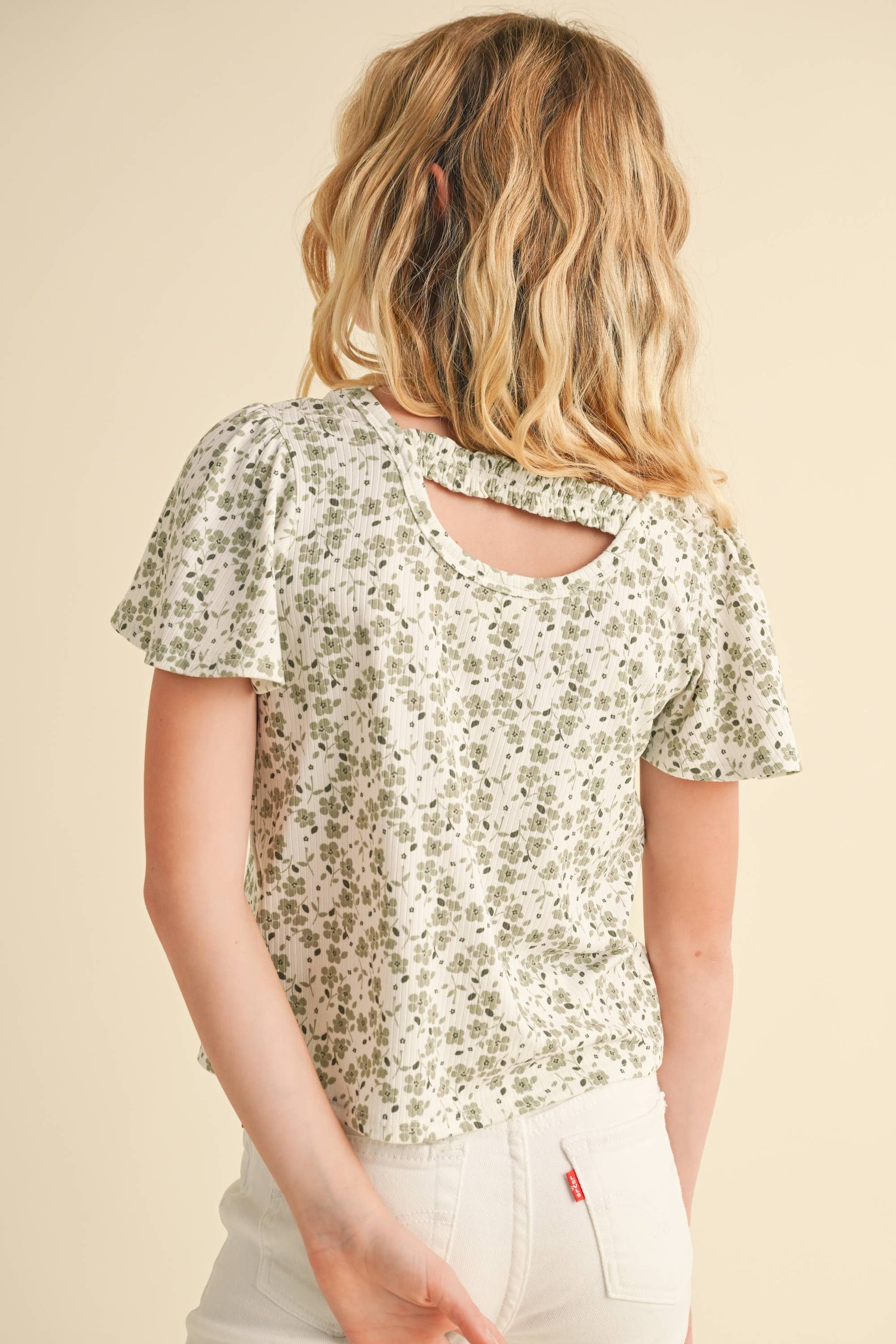 Young girl wearing a floral blouse with a cutout back design on a beige background