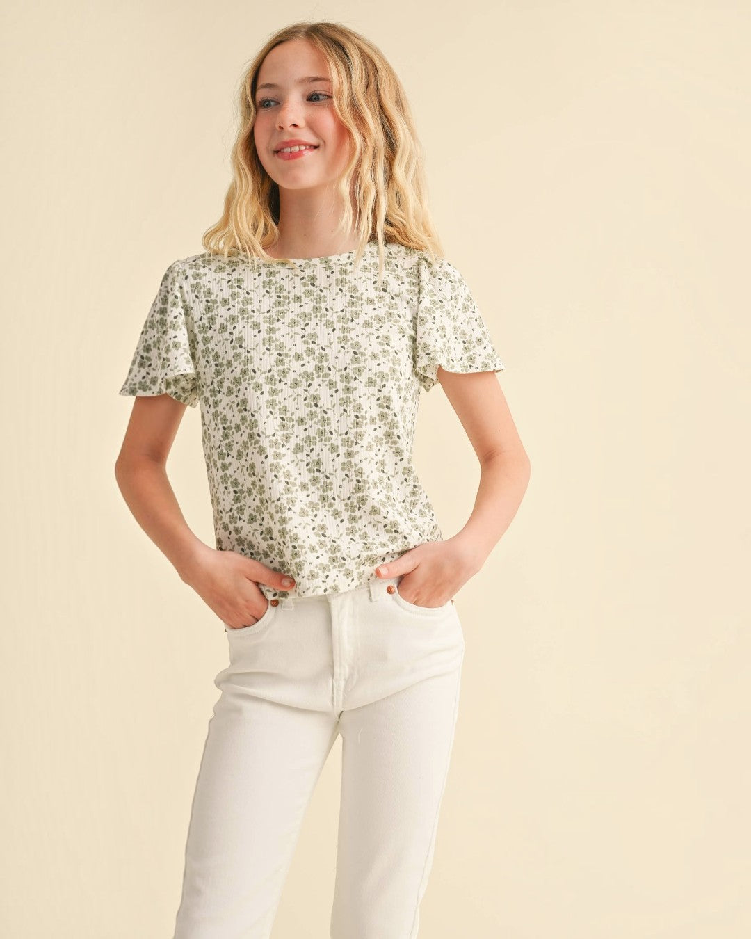 Young girl wearing a floral blouse and white pants on a beige background