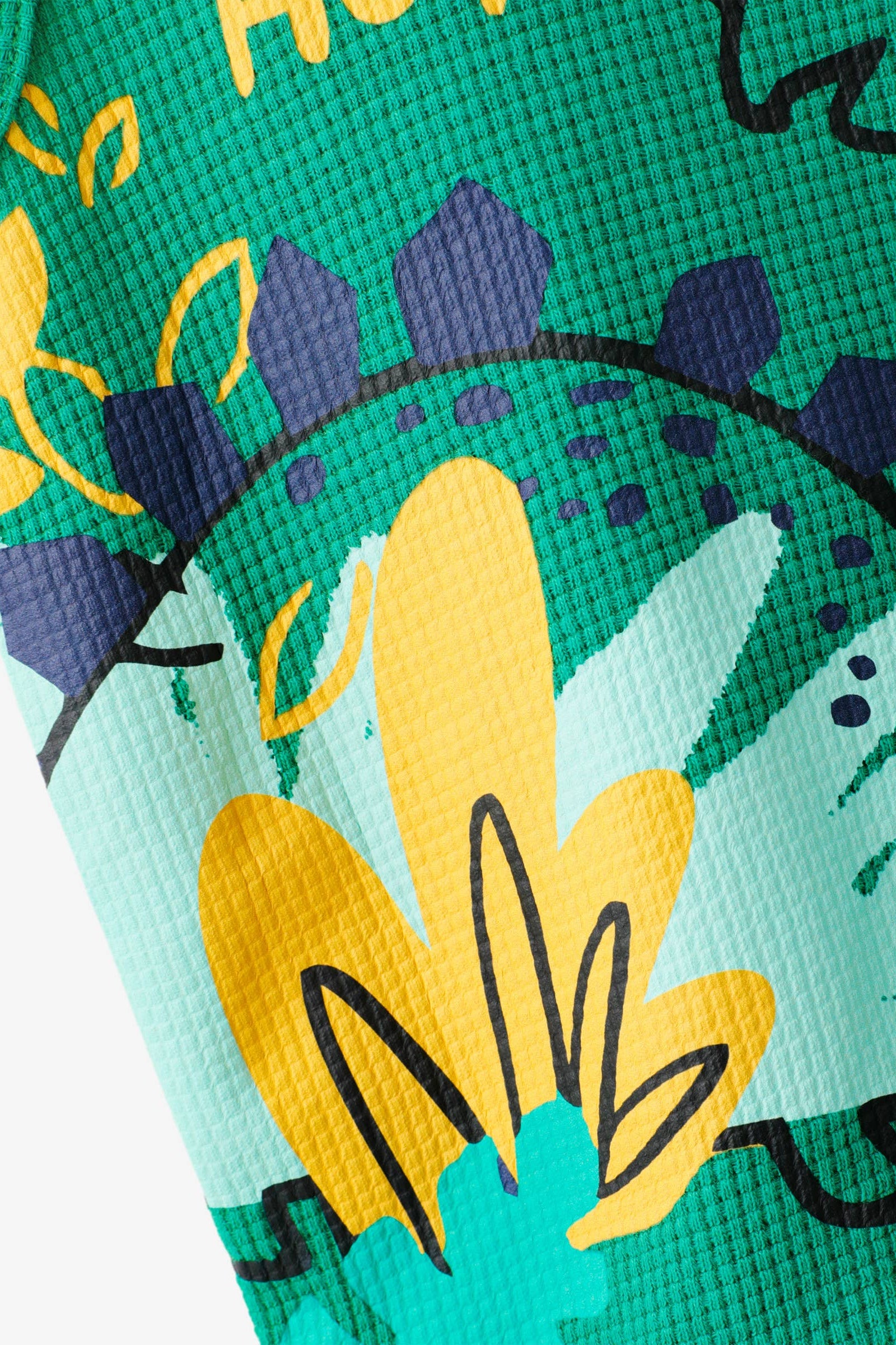 Close-up of a green fabric with yellow dinosaur illustrations and text.
