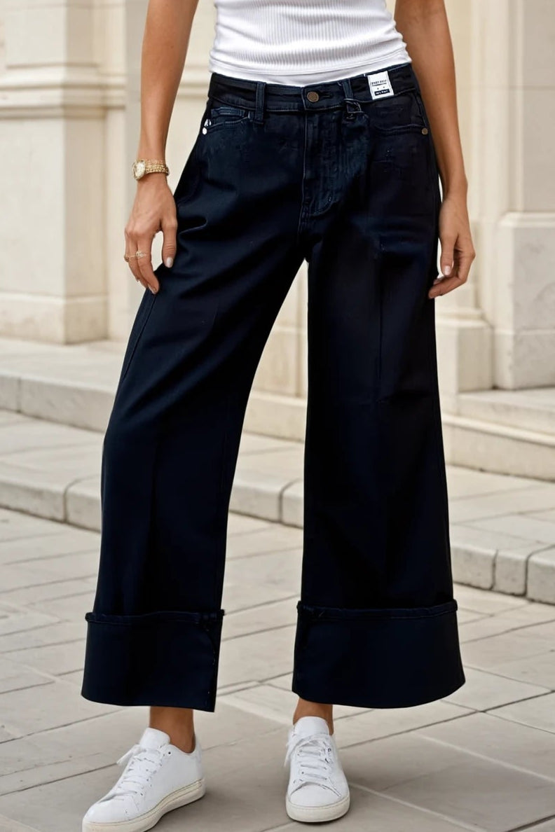 Woman wearing a white tank top and dark blue pants standing in front of a building.