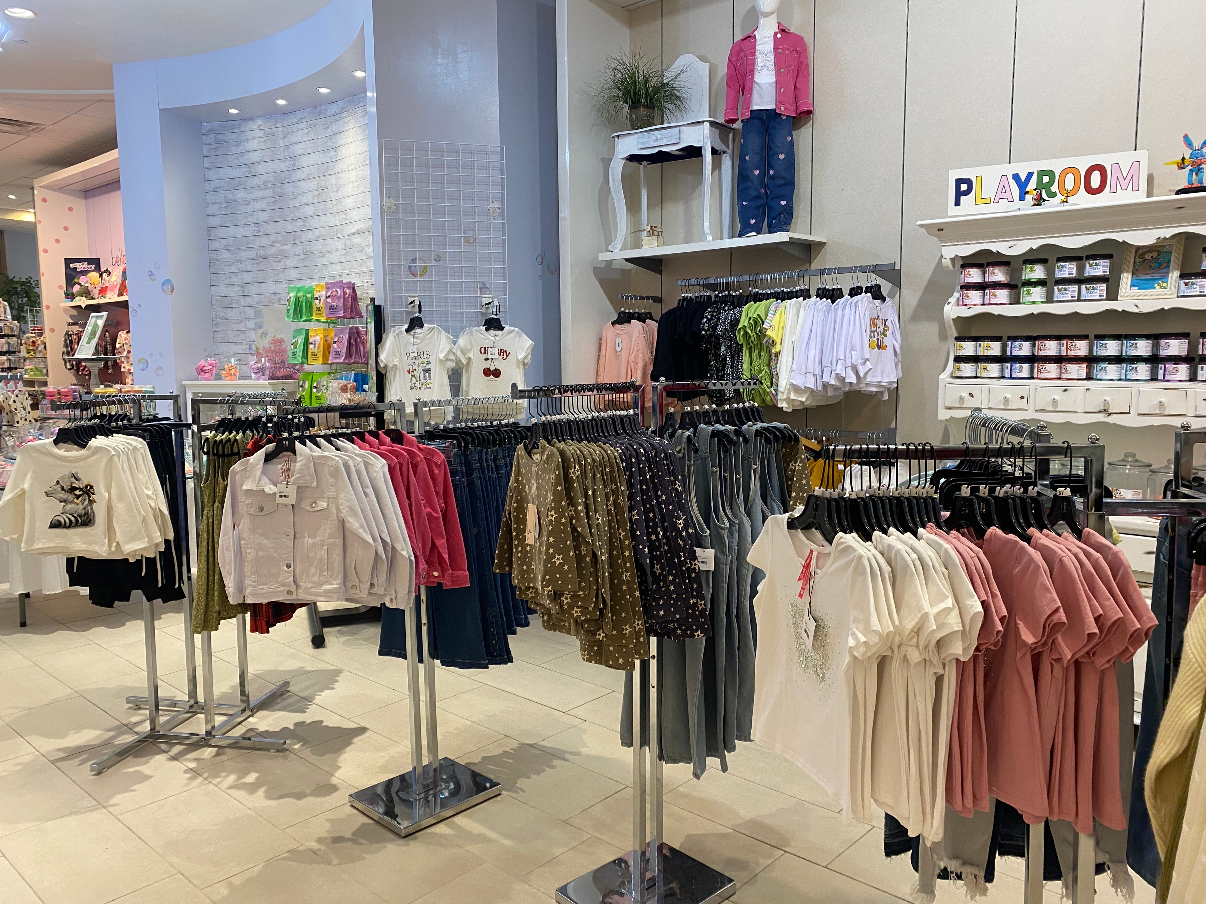 Clothing store interior with racks of clothes and a 'Playroom' sign.
