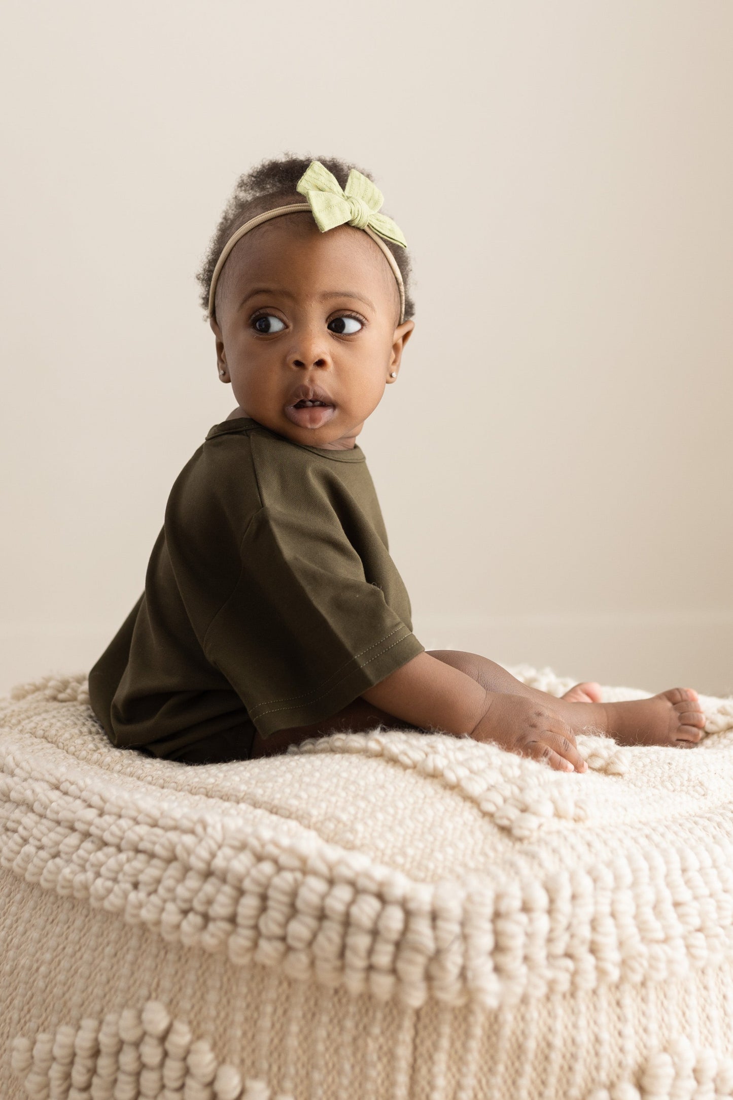 Baby sitting on a textured ottoman with a neutral background