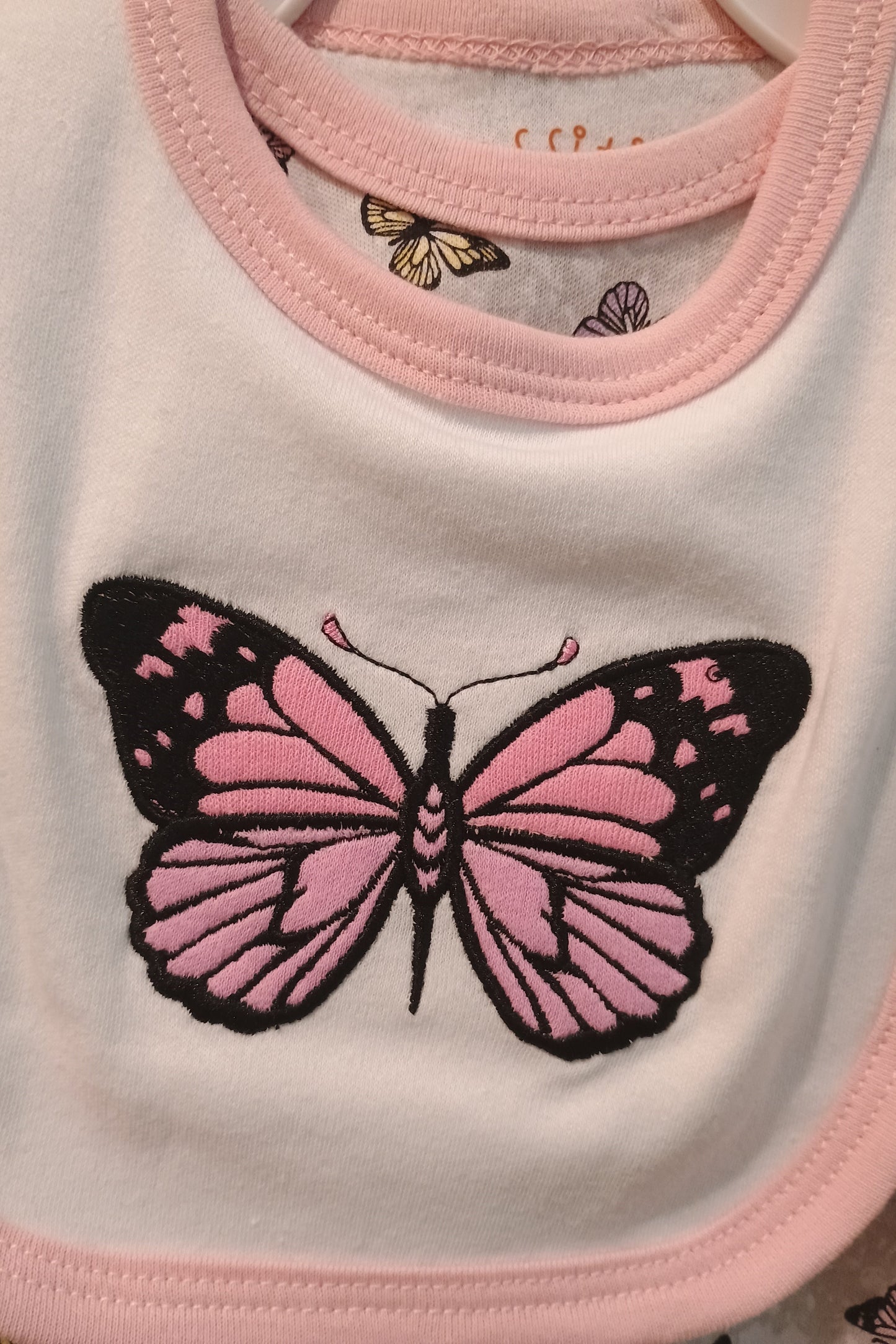 Close-up of a pink butterfly design on a white bib with pink trim.