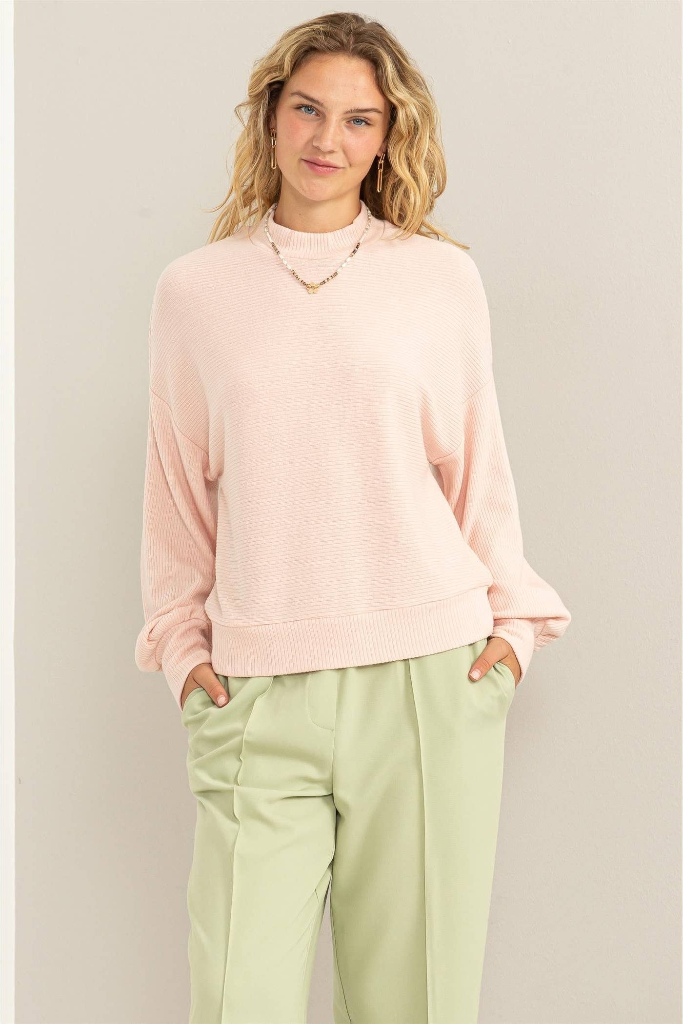 Woman wearing a light pink sweater and light green pants against a beige background