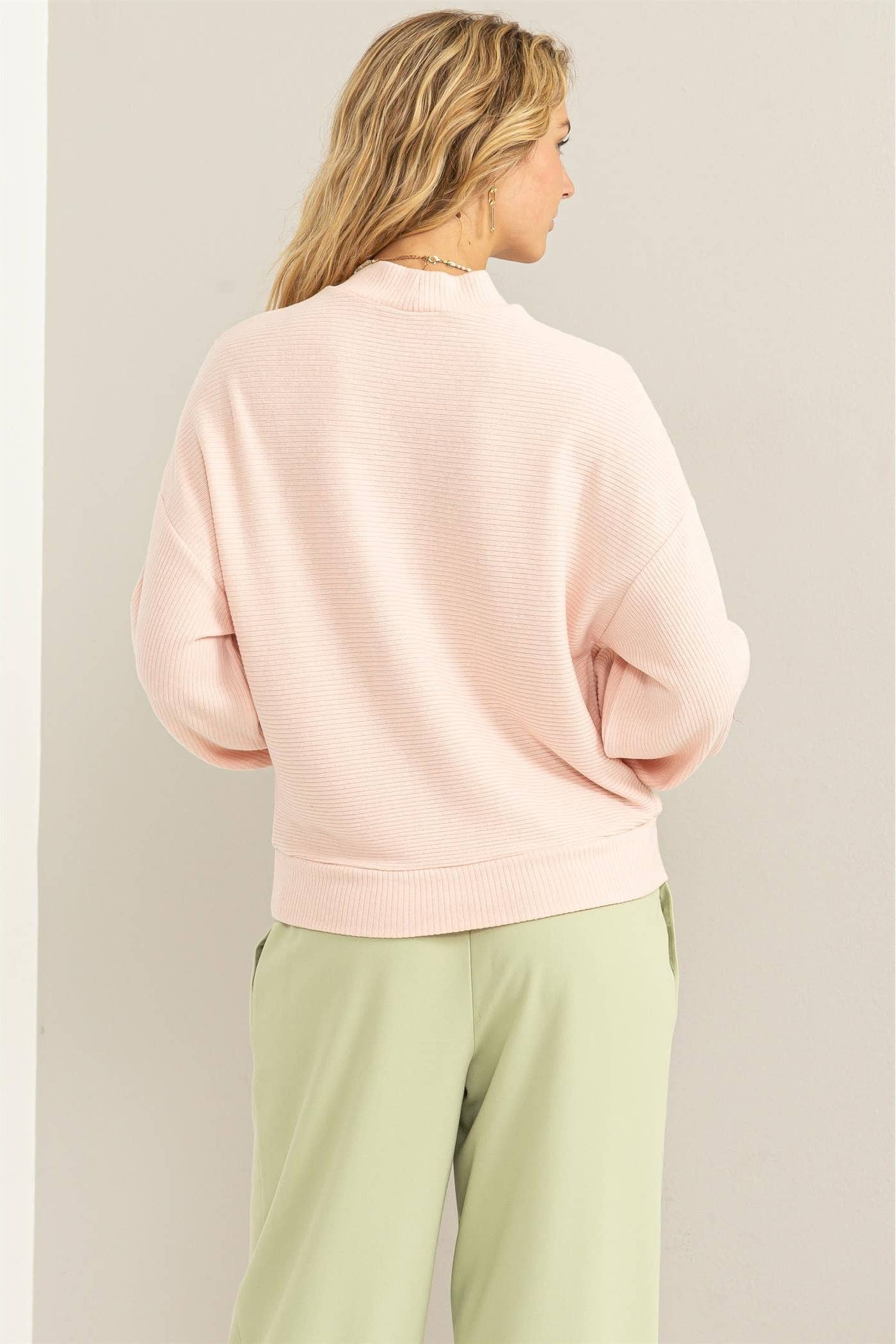 Person wearing a light pink sweater and light green pants against a plain background