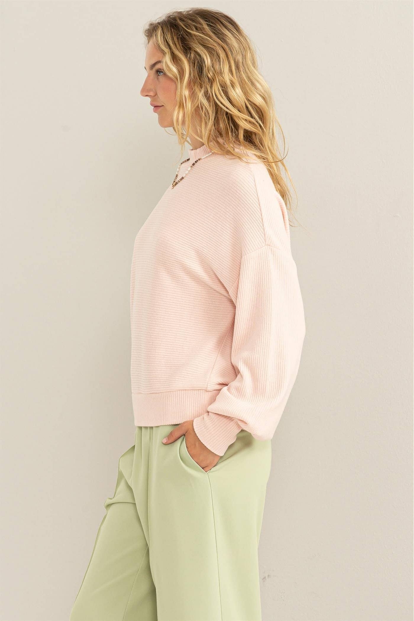 Woman wearing a pink sweatshirt and light green pants against a plain background