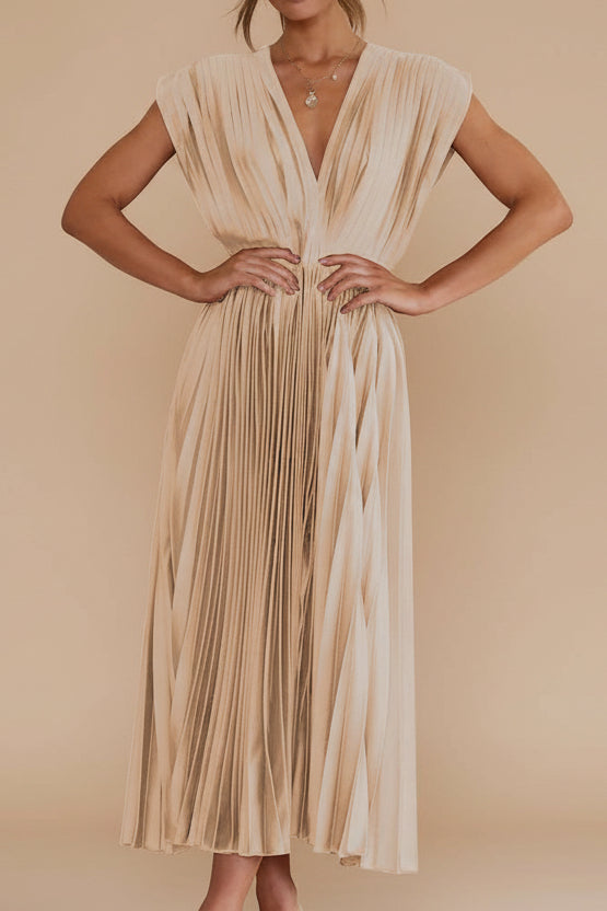 Woman wearing a gold pleated dress against a stone wall.