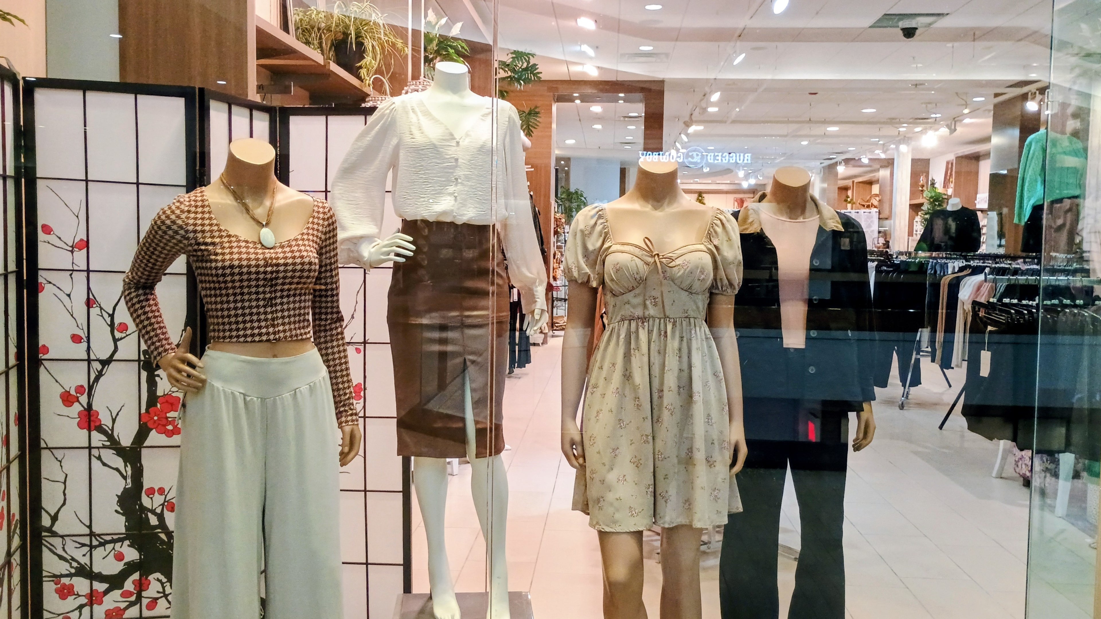 Mannequins wearing clothing in a store setting with a cherry blossom design on the wall.