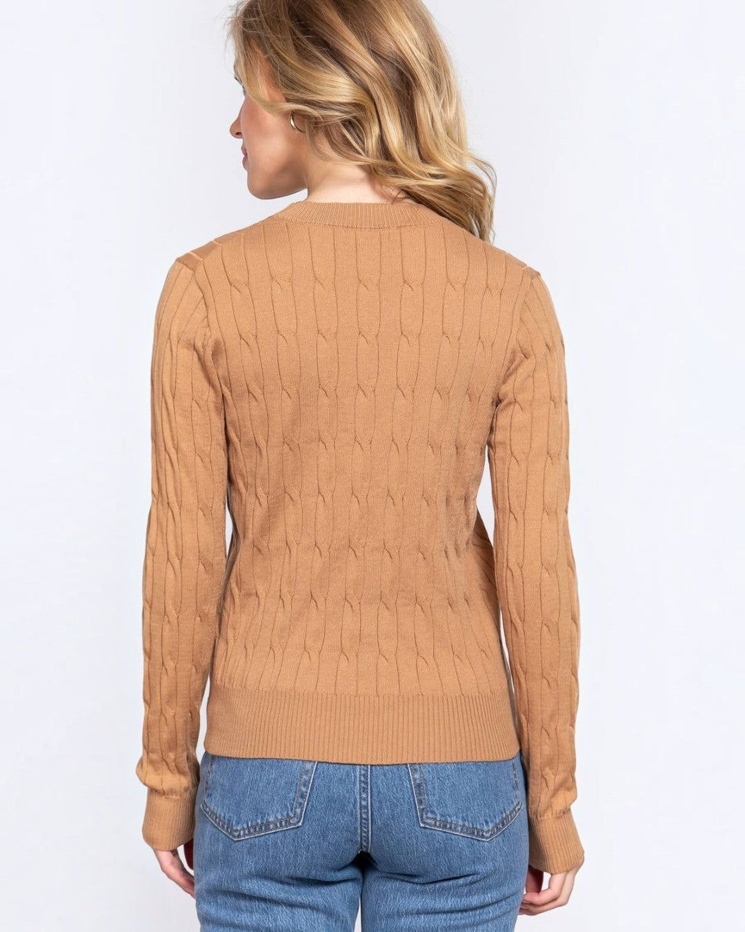 Woman wearing a brown cable knit sweater and blue jeans on a white background