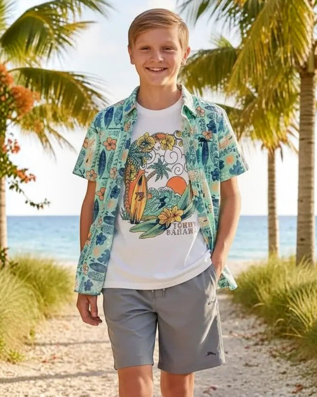 Young boy standing on a beach path with palm trees and ocean in the background