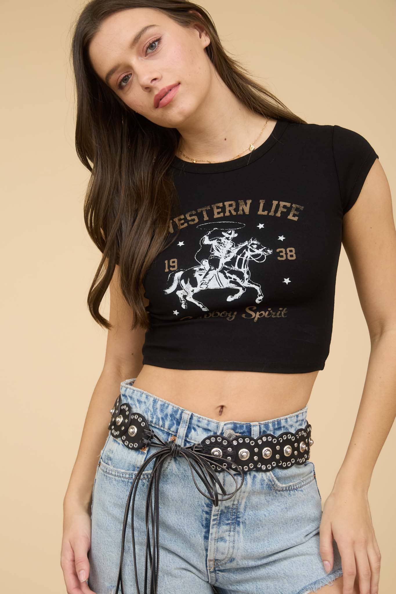 Woman wearing a black 'Western Life' crop top and denim shorts with a studded belt.