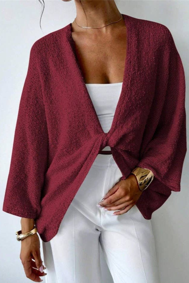 Person wearing a burgundy knitted cardigan over a white top and pants on a plain background