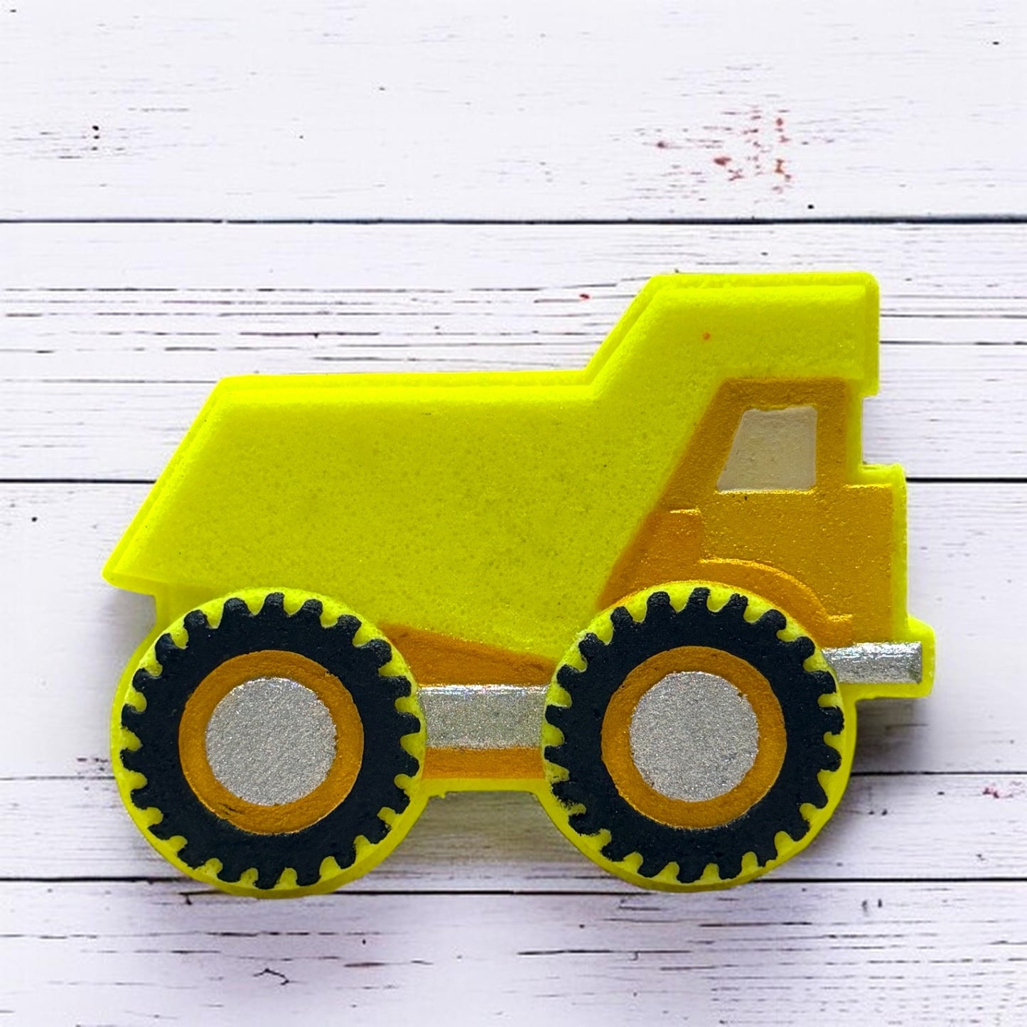 Yellow bath bomb dump truck on a white wooden surface