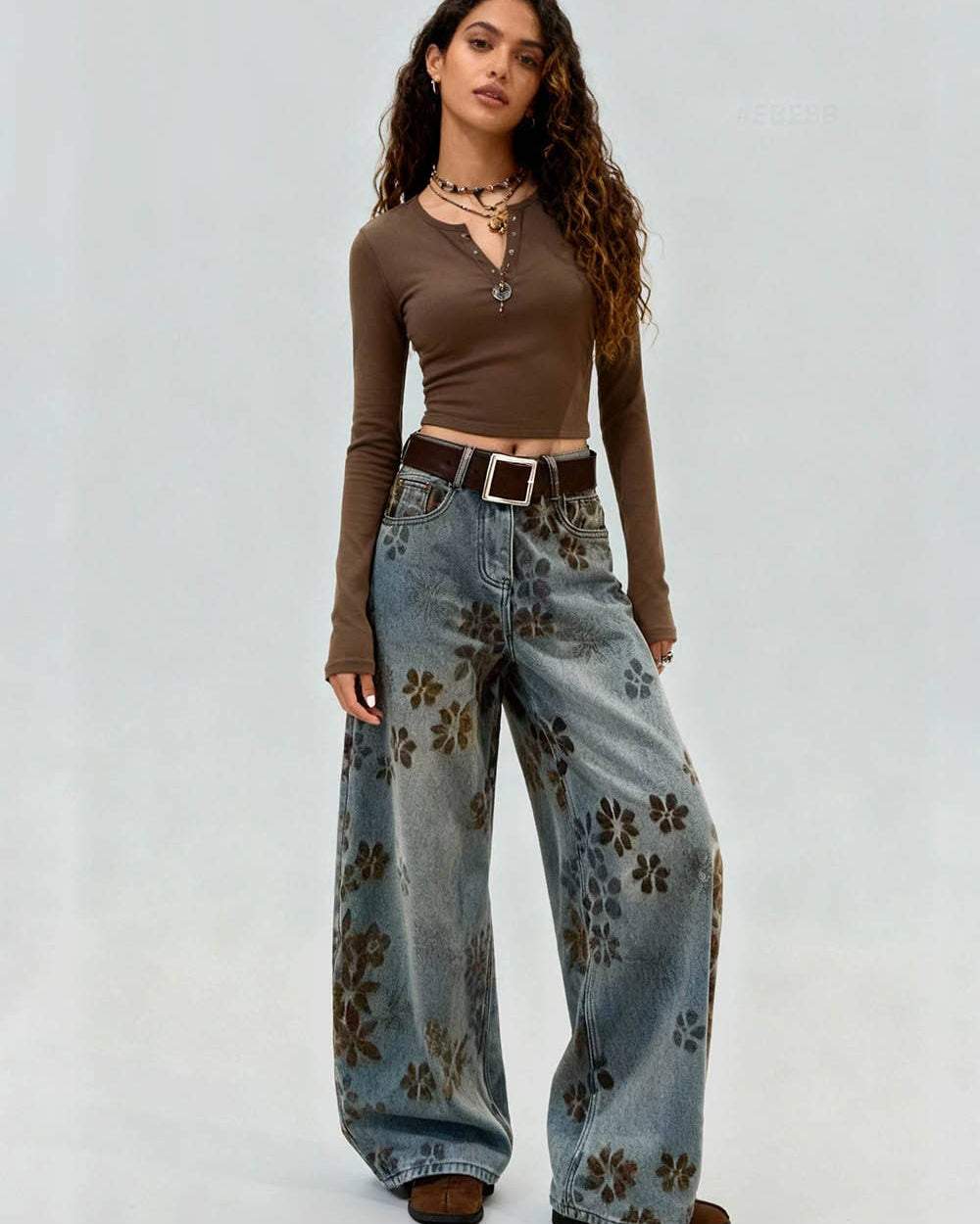 Woman wearing a brown long-sleeve top and floral jeans on a plain background