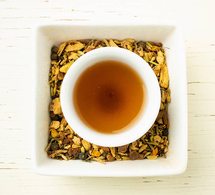 Tea cup with tea leaves and a white bowl on a light wooden surface