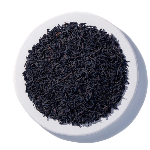 A top-down view of loose-leaf tea leaves piled in the center of a round white plate against a white background.