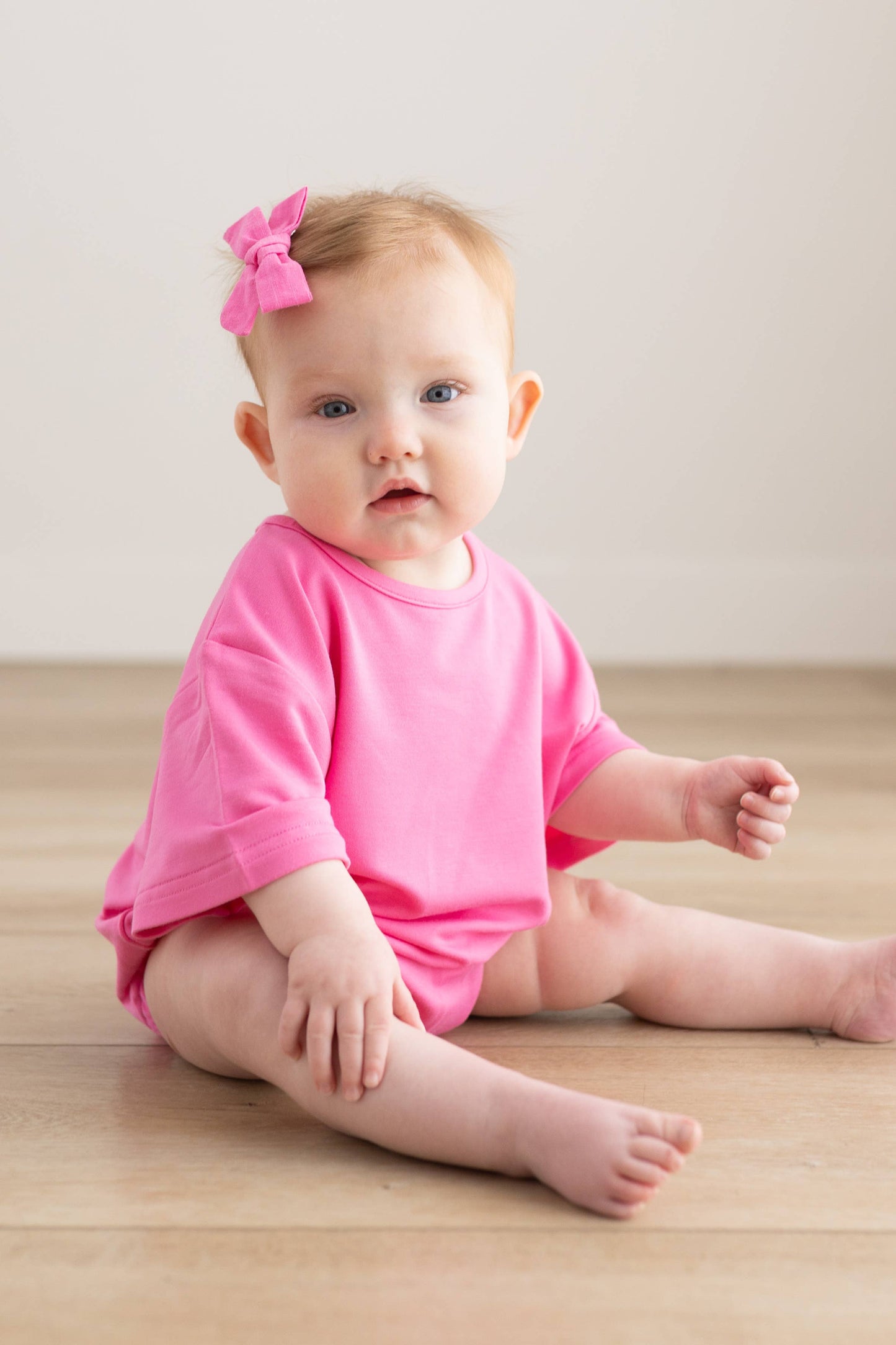 Baby in a pink outfit sitting on a wooden floor with a white background