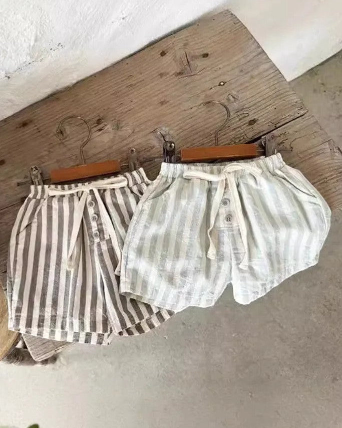Two pairs of shorts hanging on a wooden board with a plant in the background.
