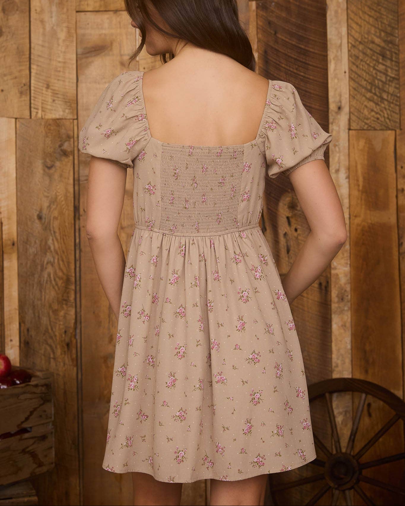 Woman wearing a floral dress standing against a wooden wall.