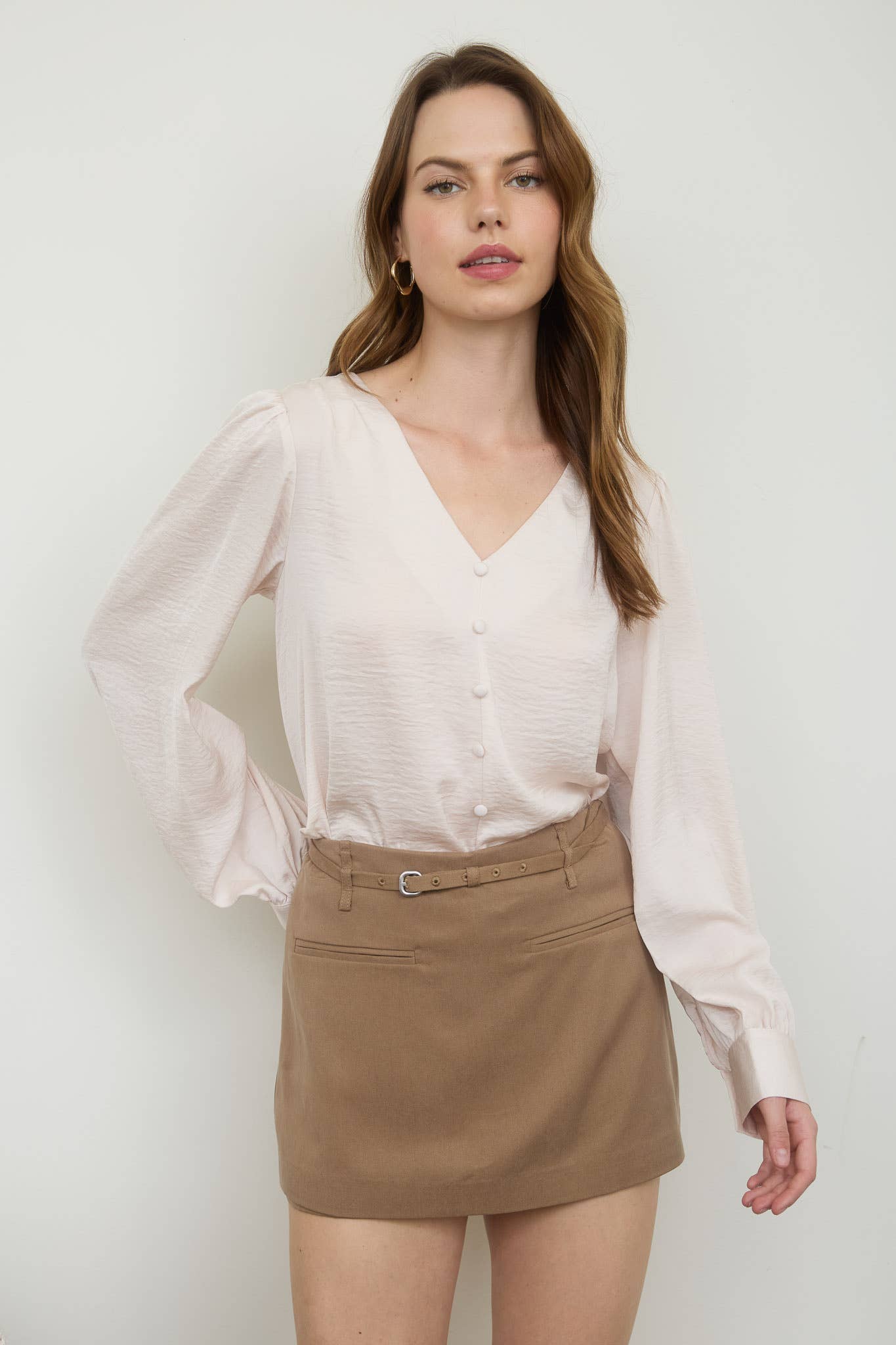 Woman wearing a white blouse with sheer sleeves and a beige skirt against a plain background