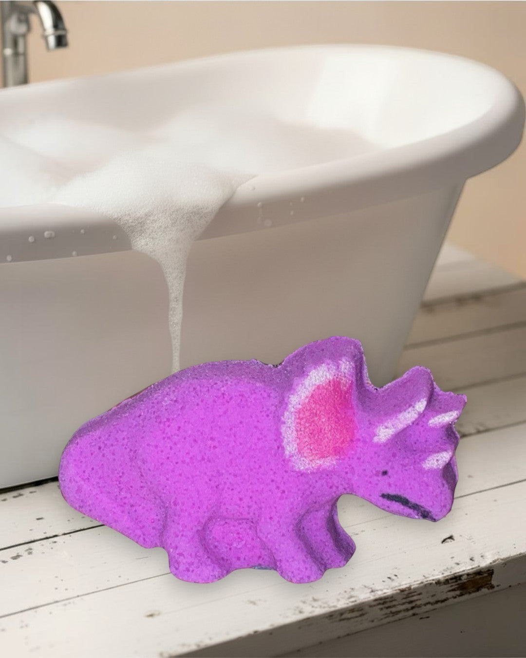 Pink dinosaur-shaped cookie on a white wooden surface