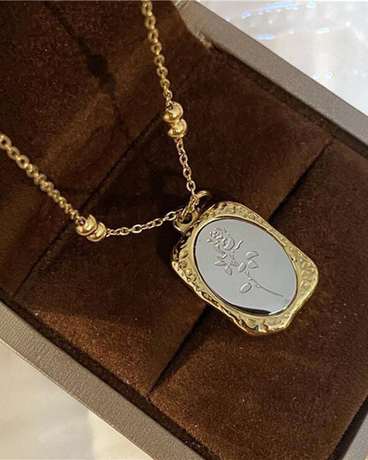 Gold necklace with a silver pendant on a brown textured surface