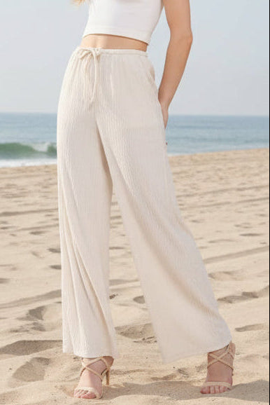 Woman wearing a white sleeveless top and beige wide-leg pants on a plain background