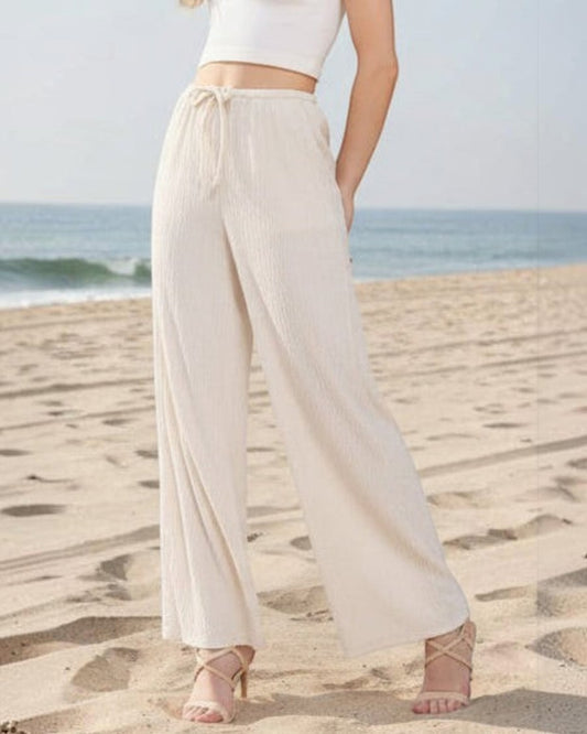 Woman wearing a white sleeveless top and beige wide-leg pants on a plain background