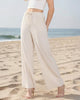 Woman wearing a white sleeveless top and beige wide-leg pants on a plain background