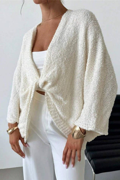 Person wearing a white textured cardigan over a white top and pants, standing against a plain background.