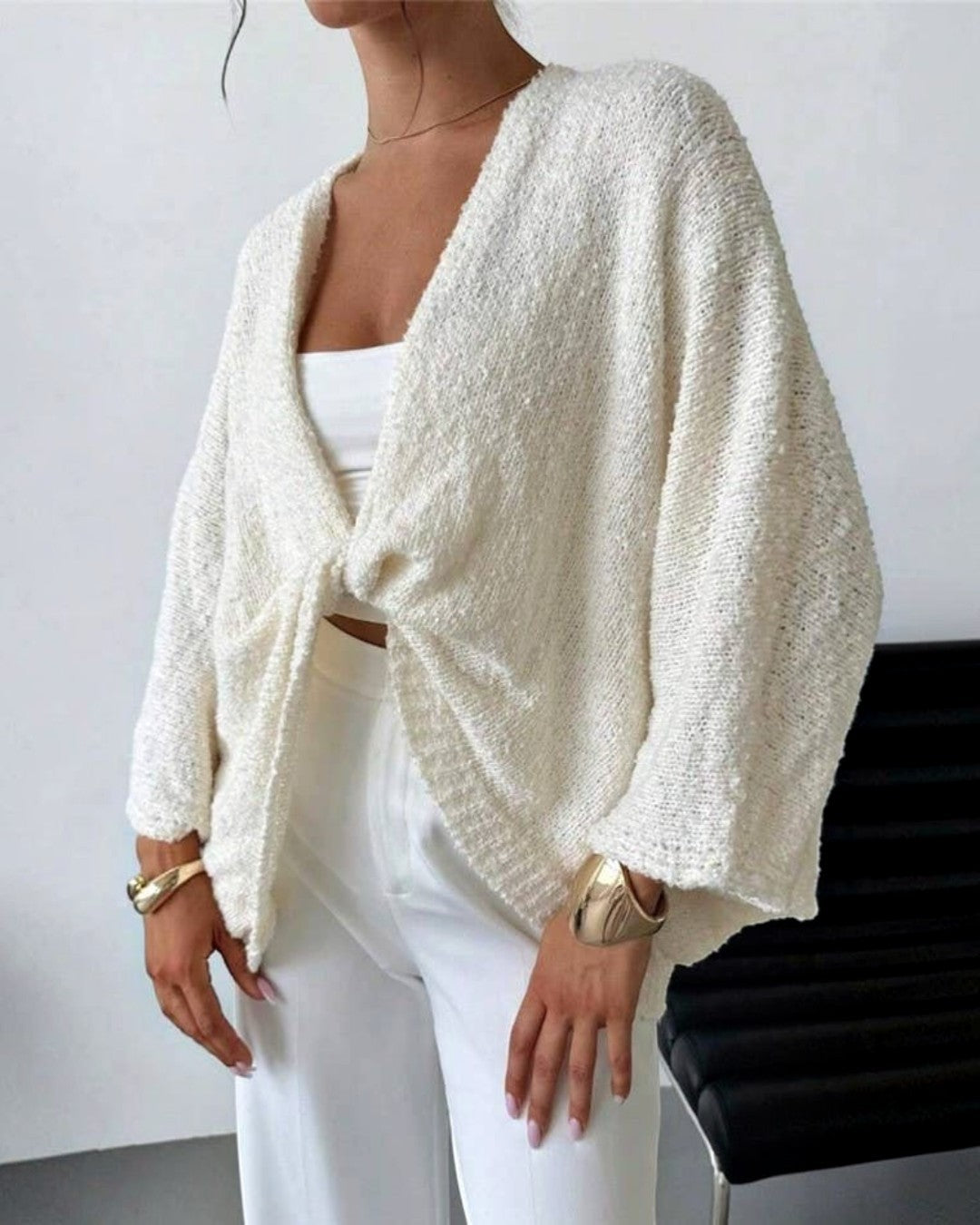 Person wearing a white textured cardigan over a white top and pants, standing against a plain background.